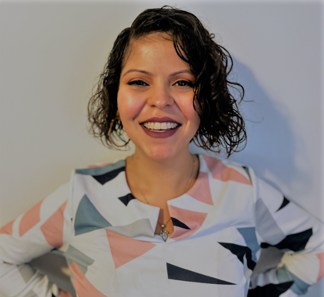 Melissa Vargas, wearing a white long sleeve top with a pink and gray geometric print, smiles in front of a white background.